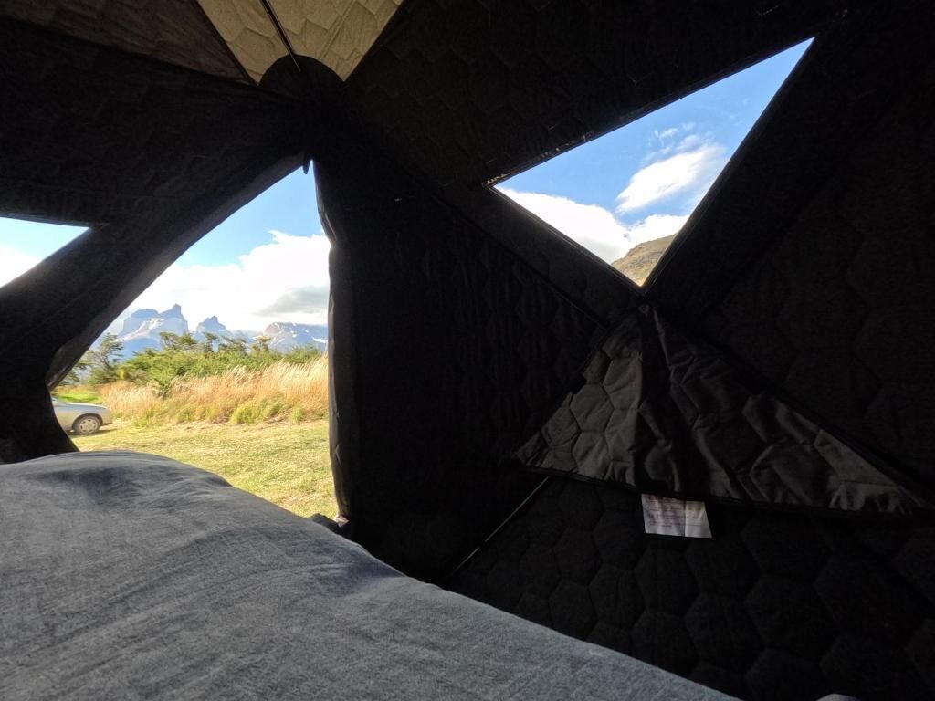 A tent with a view of mountains and a car in the background.