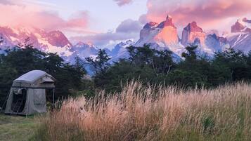 A tent in a grassy field with mountains in the background.