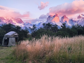 Una tenda in un prato erboso con montagne sullo sfondo.