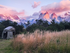 A tent in a grassy field with mountains in the background.