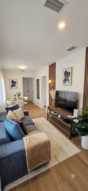 Een moderne woonkamer met een bank, een televisie en een eethoek op de achtergrond.