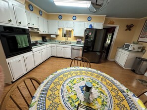 A kitchen with white cabinets, a microwave, a refrigerator, and a dining table with a floral tablecloth.