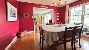 Uma sala de jantar com uma mesa posta para quatro pessoas, cadeiras de madeira, um lustre e uma parede vermelha.