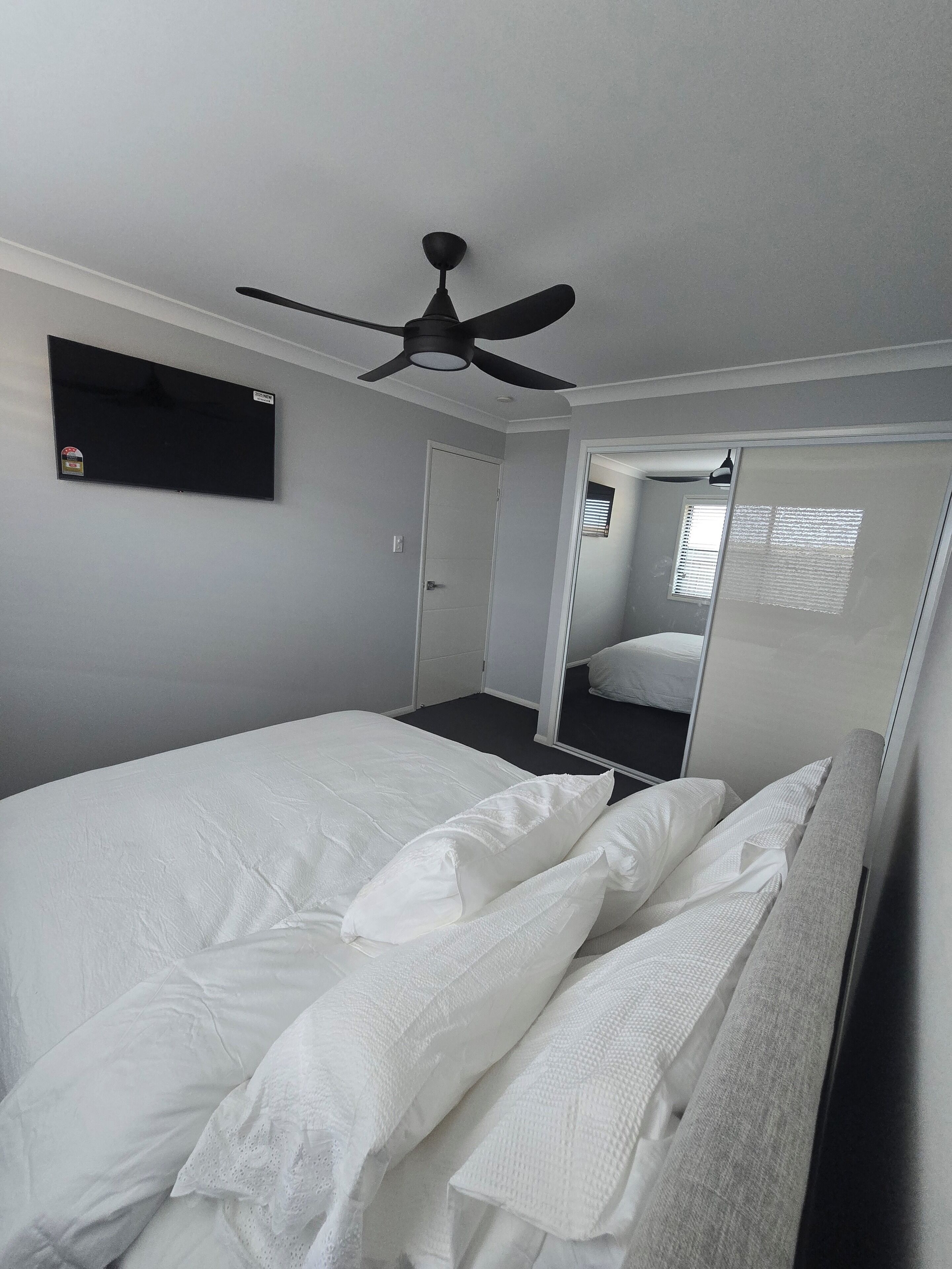 Une chambre à coucher avec un lit, un ventilateur de plafond, un téléviseur à écran plat et un miroir.