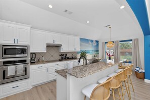 A modern kitchen with white cabinetry, a granite countertop, and a large island with bar stools. - 5-BD/3-BA Spacious Getaway | Pool, Golf Sim & More (Burleson)