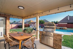 An outdoor patio with a grill, table, and chairs. - 5-BD/3-BA Spacious Getaway | Pool, Golf Sim & More (Burleson)