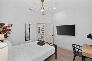 A bedroom with a bed, a desk with a chair, a flat-screen TV, a ceiling fan, and a mirror. - 5-BD/3-BA Spacious Getaway | Pool, Golf Sim & More (Burleson)