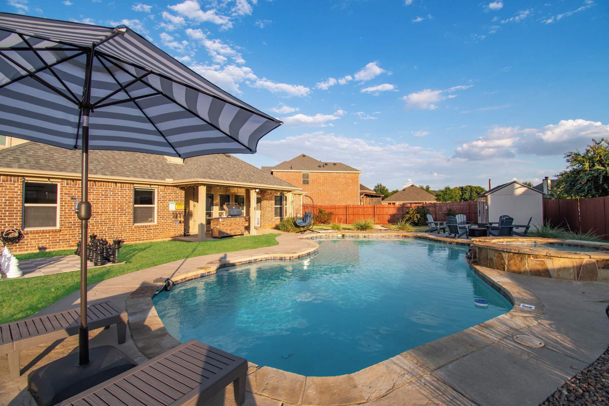A backyard with a swimming pool, a covered patio area, and a brick house.
