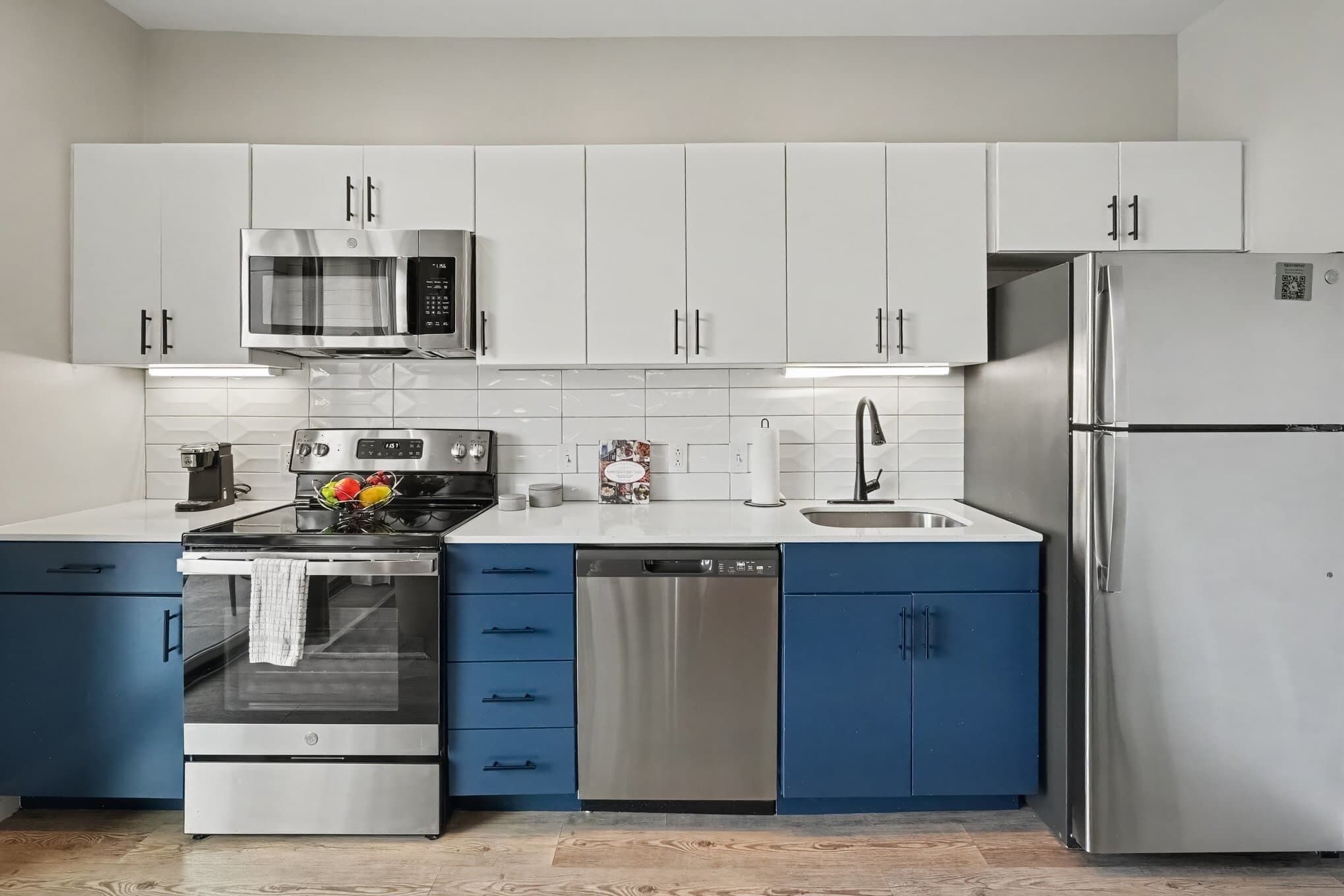 Una cocina moderna con electrodomésticos de acero inoxidable, armarios blancos y detalles en azul.