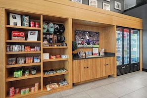 A snack bar with shelves stocked with various packaged snacks, a counter with a beverage dispenser, and a refrigerator with drinks. - Verse - Pool & Gym - Mins to Broadway (Nashville)