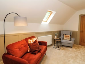 An attic room with a red sofa, a checkered armchair, a small table with a vase, and a skylight. - Nevis Bridge House (Fort William)