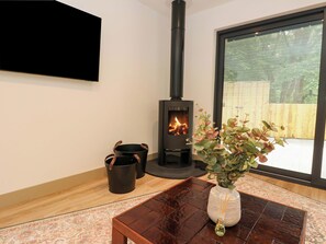 Una habitación con estufa de leña, un ventanal grande y una mesa con un jarrón de flores.