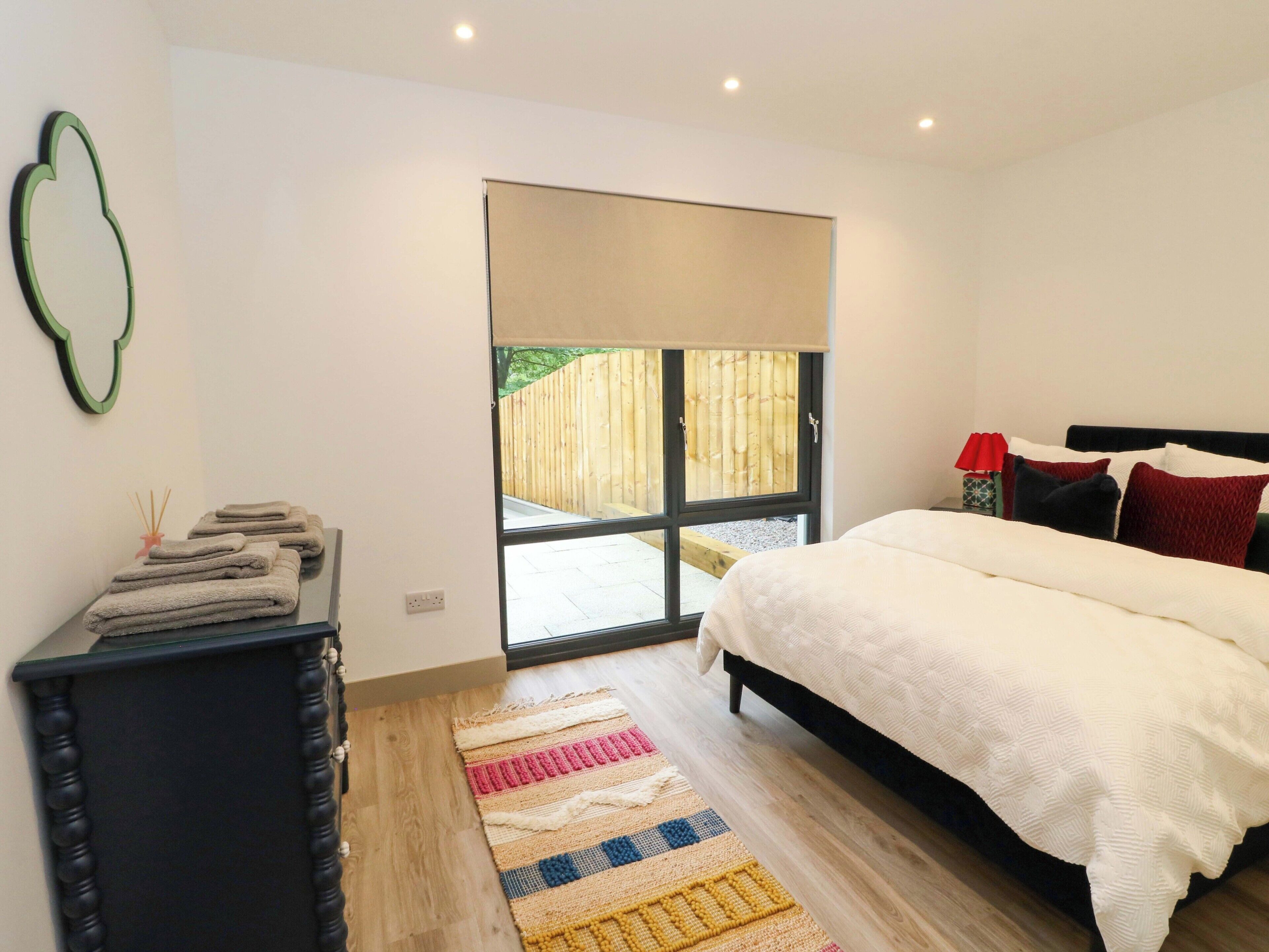 Un dormitorio con cama, mesita de noche, espejo, ventana y puerta.
