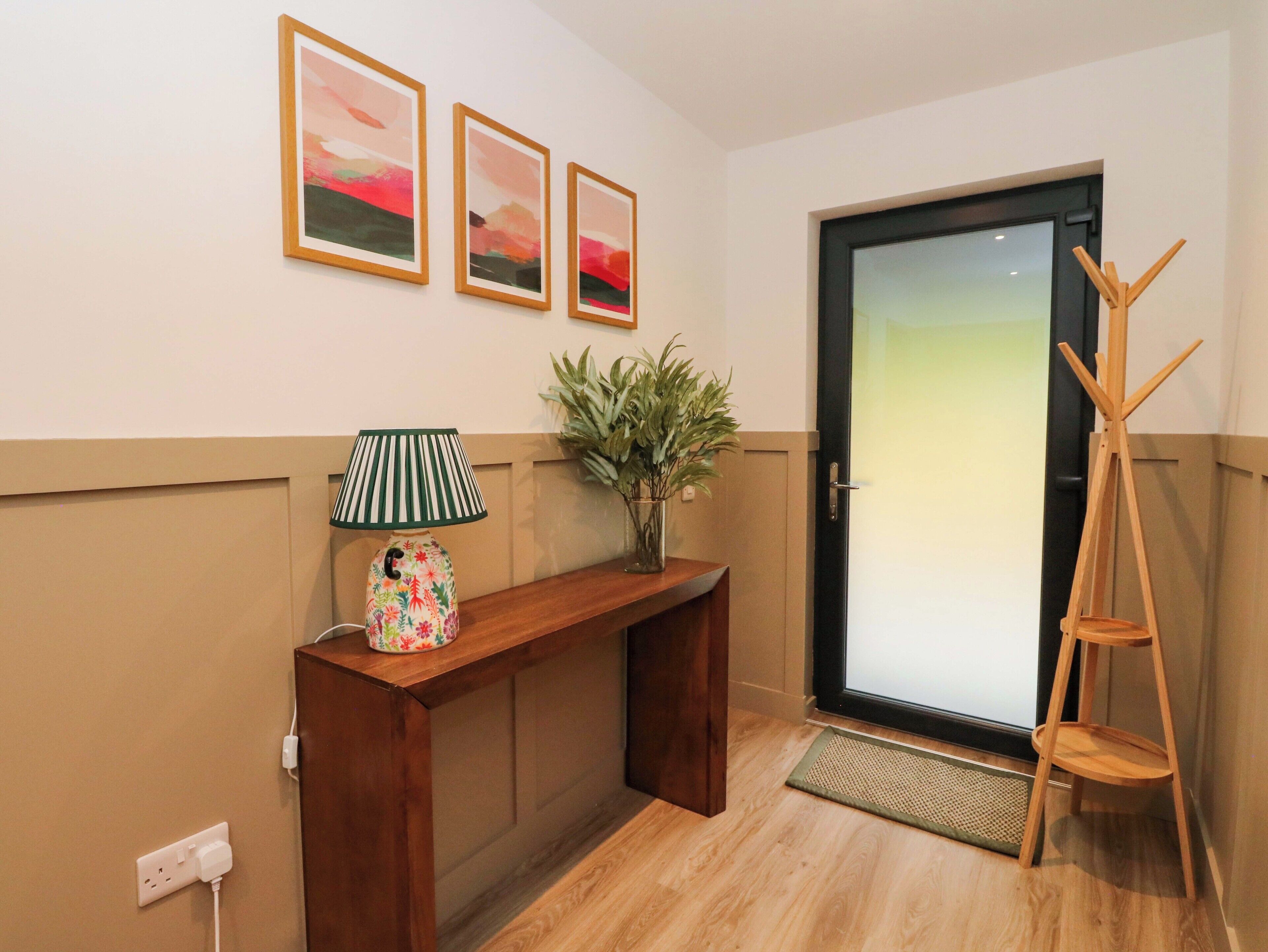 A hallway with a wooden console table, a lamp, a plant, and three framed pictures on the wall.