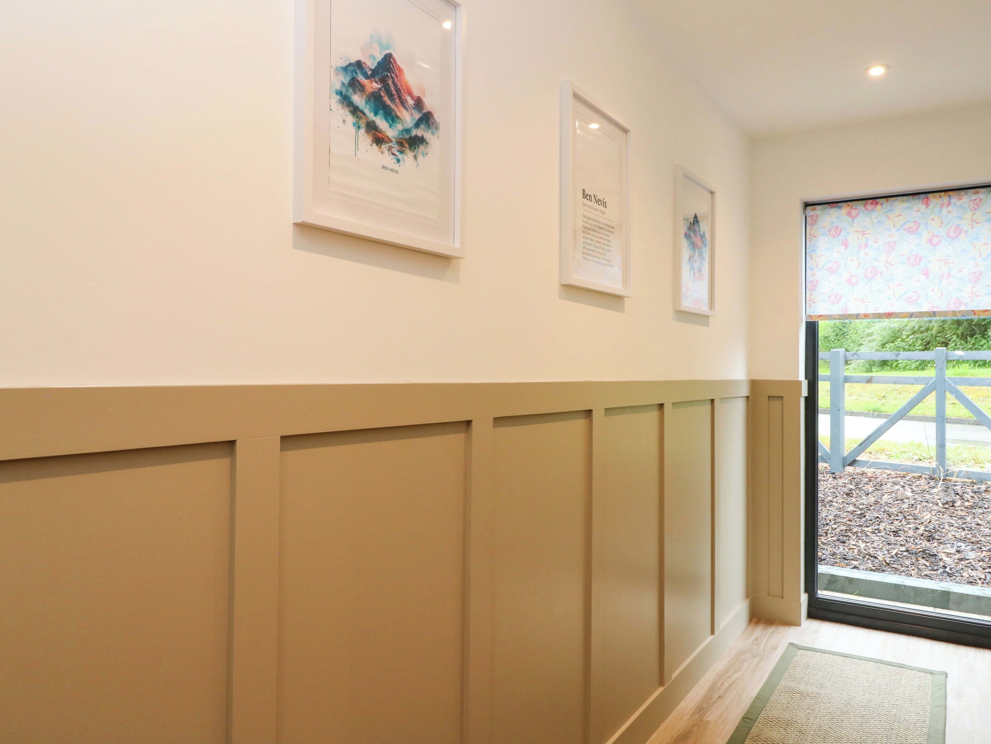 A hallway with framed artwork on the wall, a wooden floor, and a door leading outside.