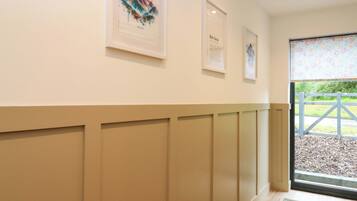 A hallway with framed artwork on the wall, a wooden floor, and a door leading outside.