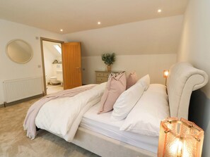 Un dormitorio con cama, mesita de noche, lámpara y una puerta que da a otra habitación.