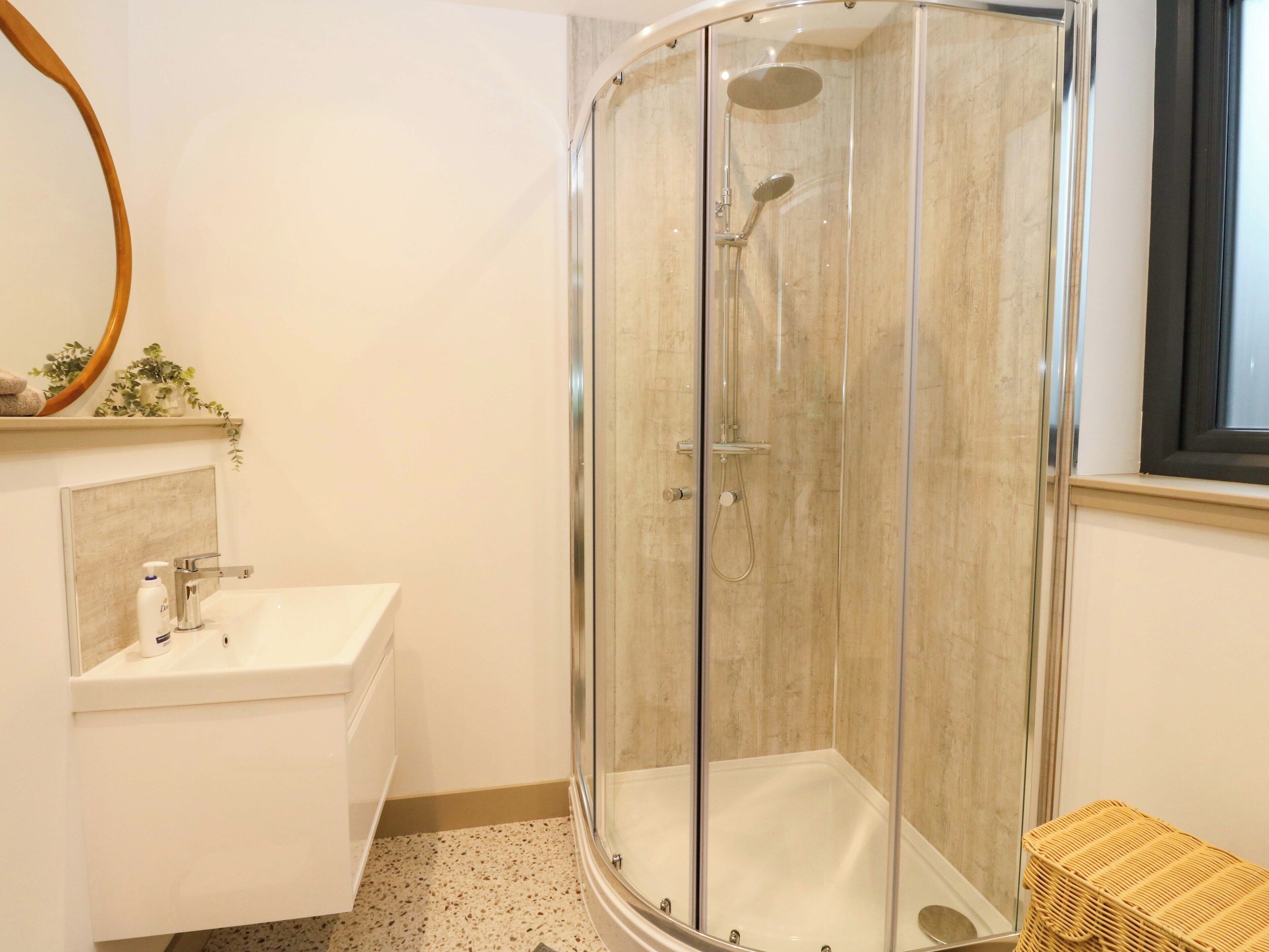 A bathroom with a glass-enclosed shower, a sink, and a small wicker stool.