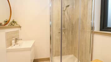 A bathroom with a glass-enclosed shower, a sink, and a small wicker stool.