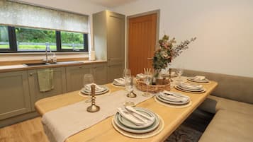 A dining area with a long table set for a meal, a window with a view of greenery, and a wooden door.