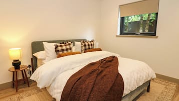 A neatly made bed with a brown throw blanket, a bedside lamp, and a window with a view of trees.