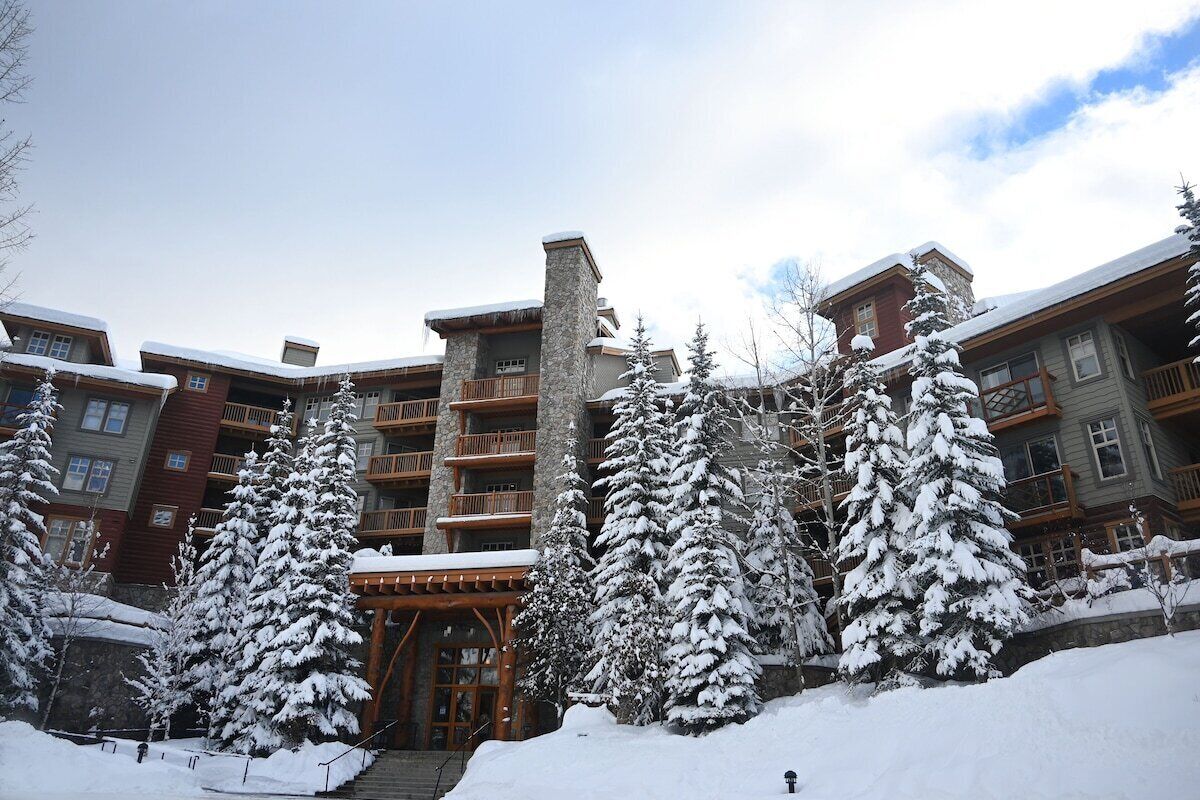 A multi-story hotel with a stone facade, wooden balconies, and snow-covered trees.