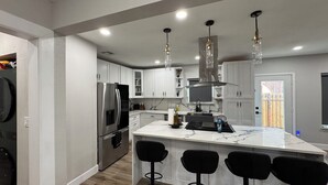 A modern kitchen with a central island, bar stools, stainless steel appliances, and pendant lighting. - Houston House 5 mins TMC, & Near NRG/Downtown (Houston)