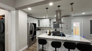 A modern kitchen with a central island, bar stools, stainless steel appliances, and pendant lighting. - Houston House 5 mins TMC, & Near NRG/Downtown (Houston)