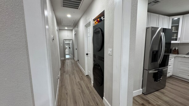 A hallway with a laundry area, including a washing machine and dryer, leading to a kitchen with a refrigerator. - Houston House 5 mins TMC, & Near NRG/Downtown (Houston)