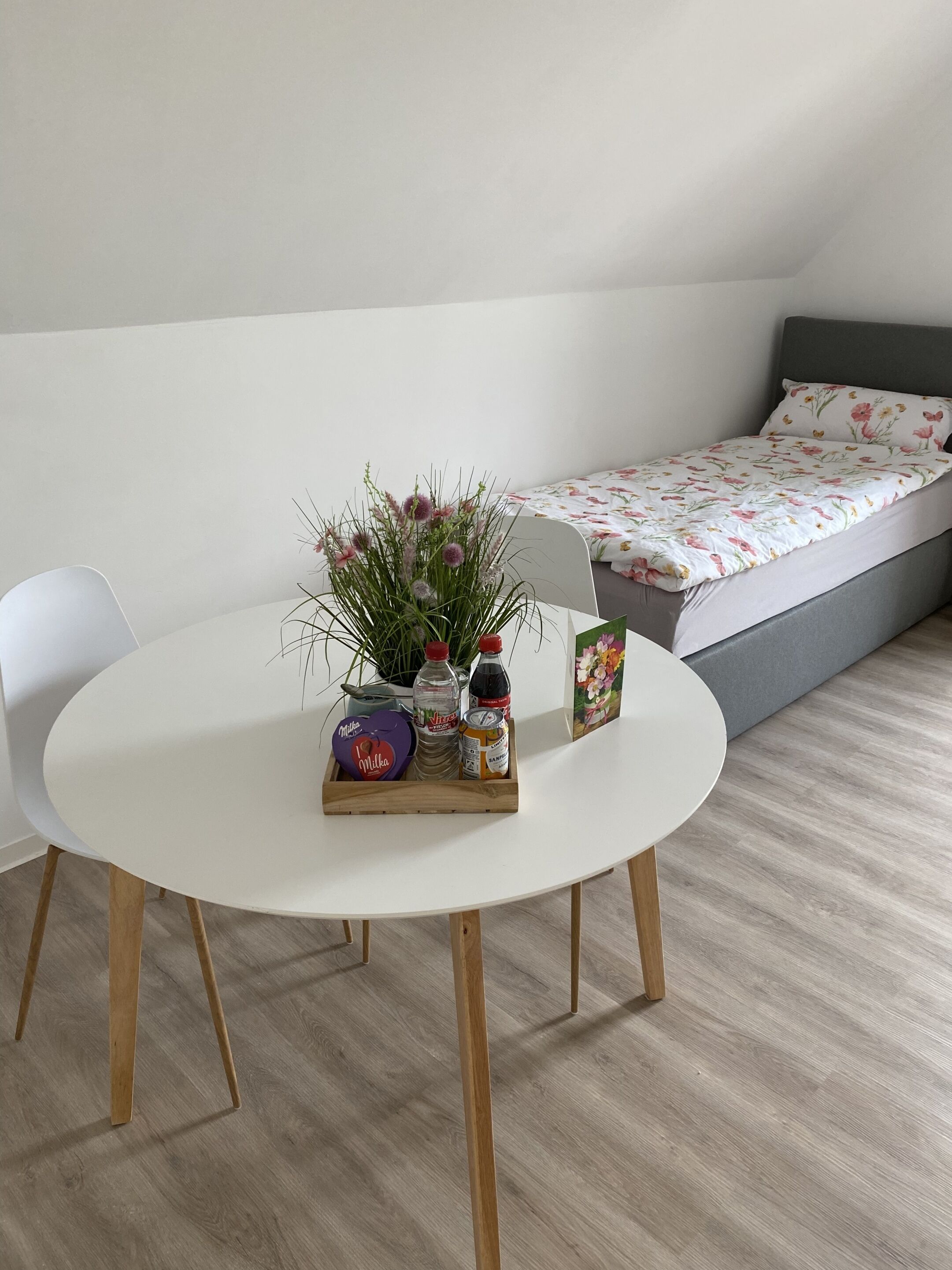 A room with a round white table, a small potted plant, and a bed with floral bedding.