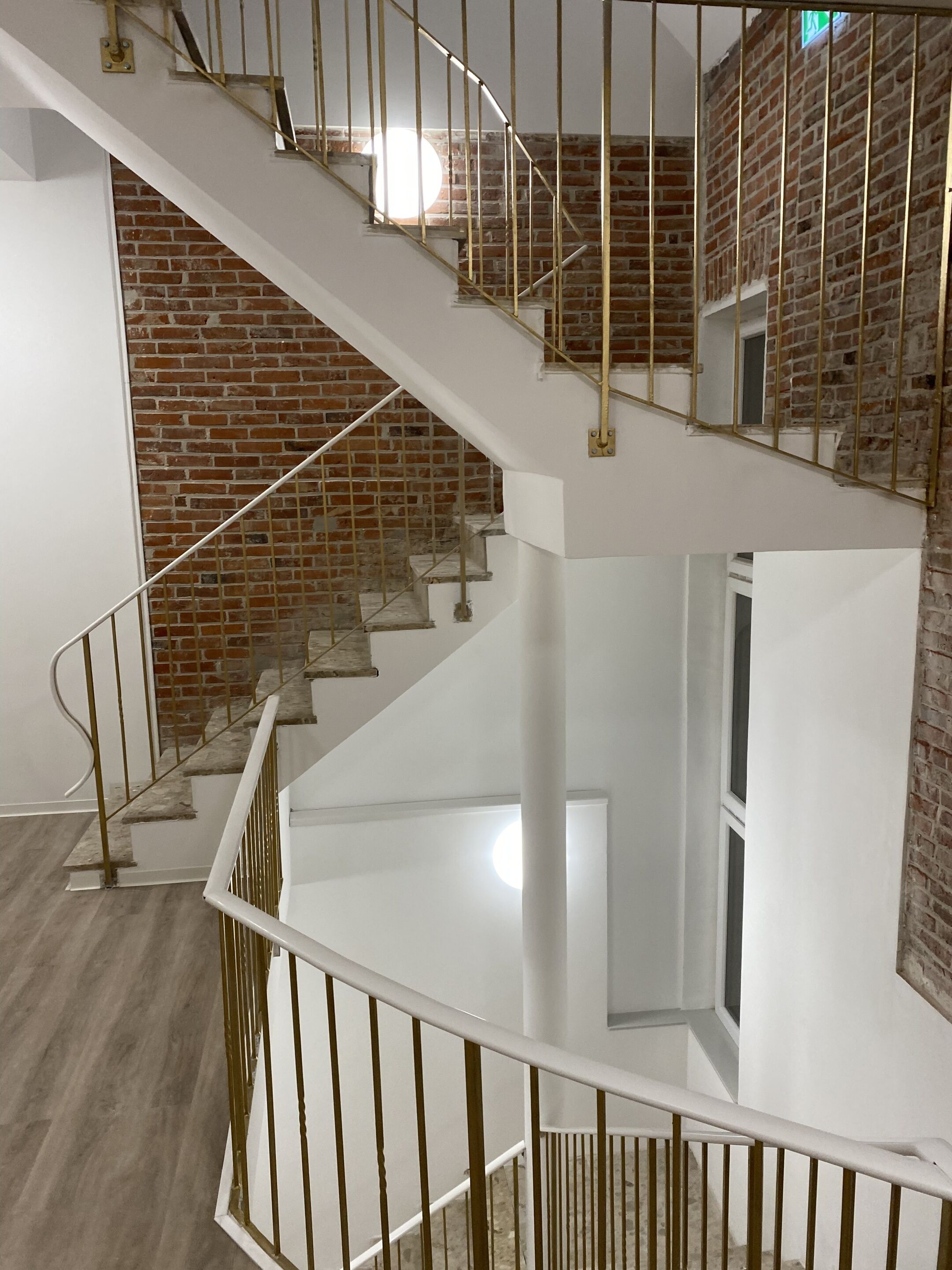 A multi-level interior with a staircase, white walls, and a brick wall.