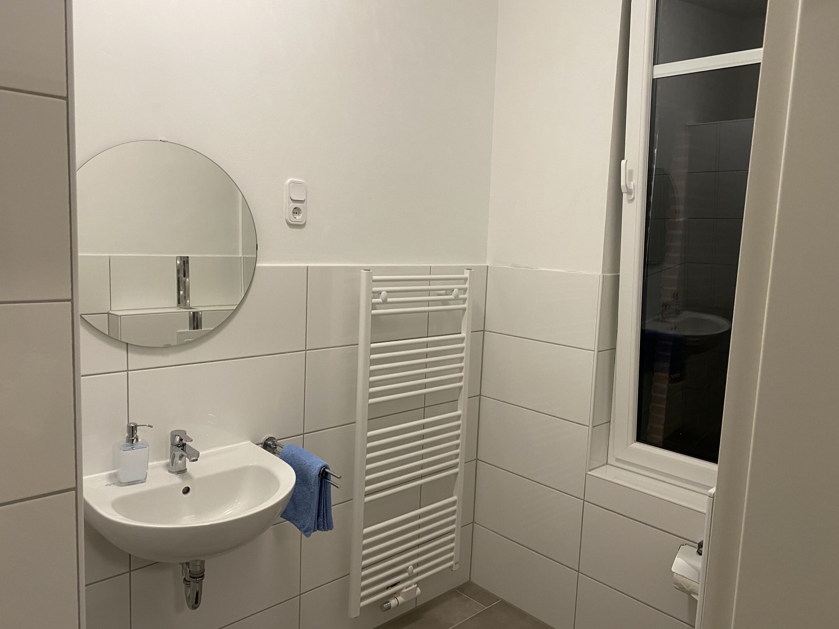 Un baño con un lavabo blanco, espejo y perchero.