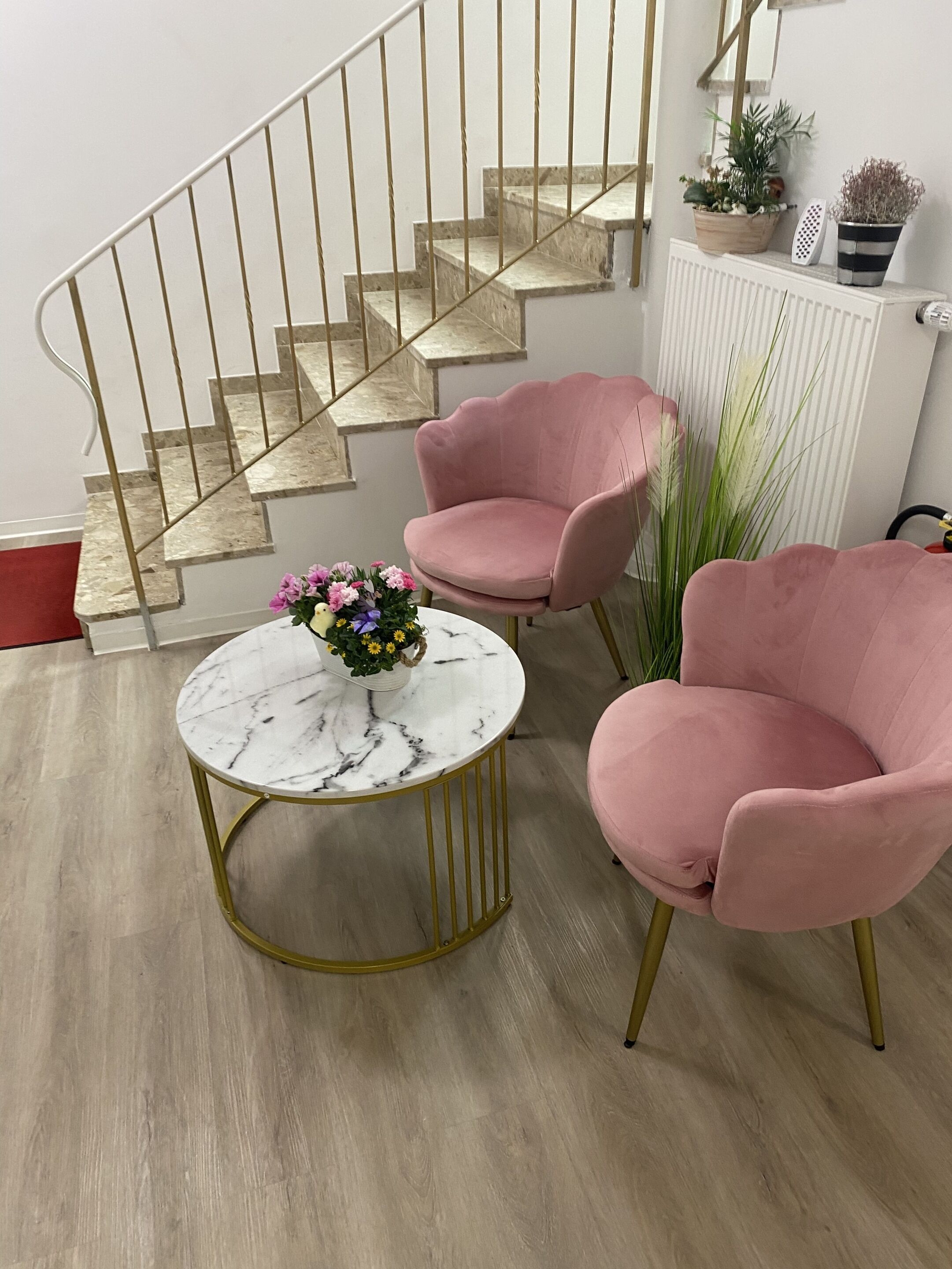 A staircase with a railing, a round marble table with a flower arrangement, and two pink chairs.