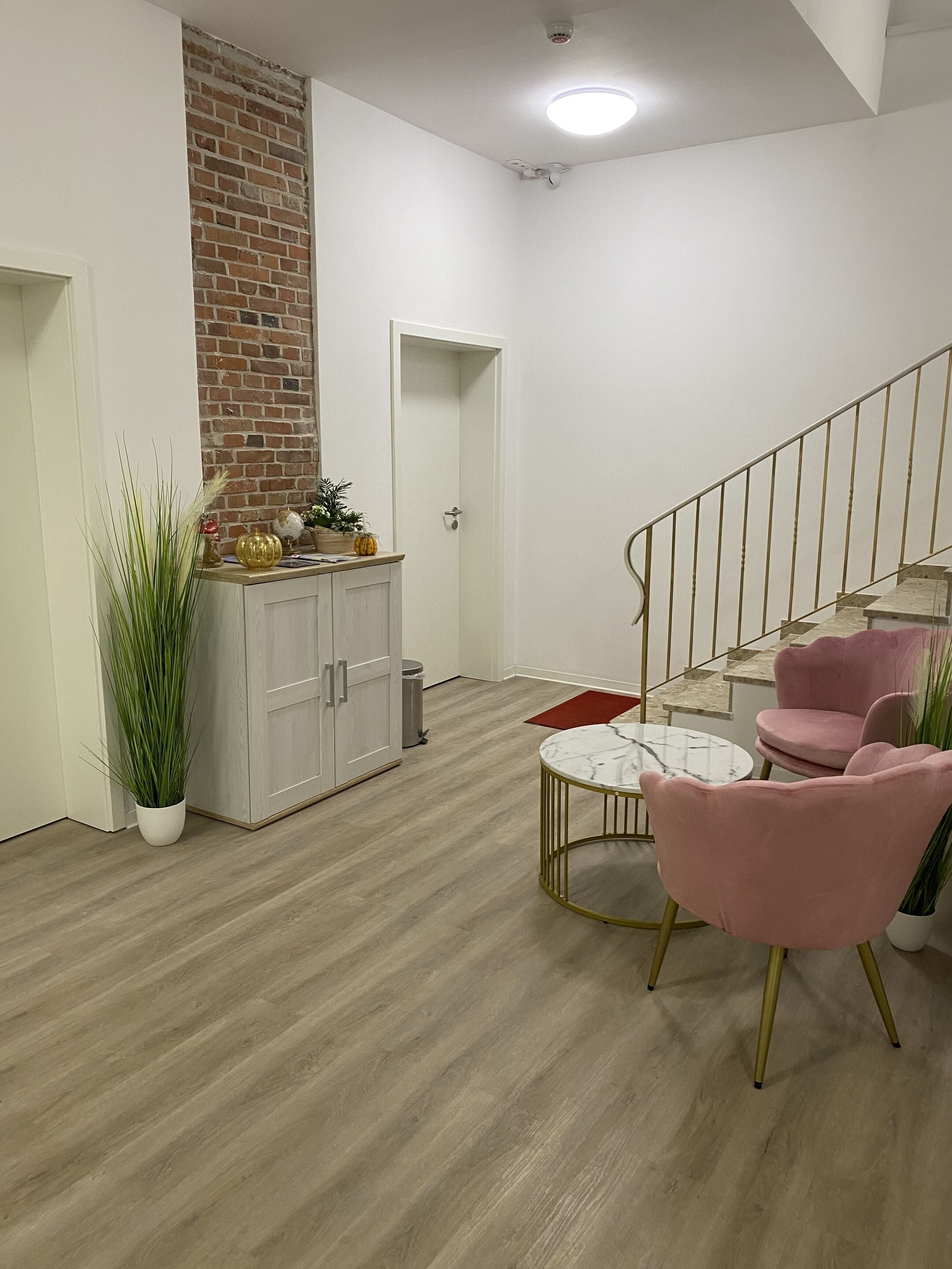 A modern living space with a staircase, a dining area with a marble table, and a kitchen with a brick wall and white cabinets.