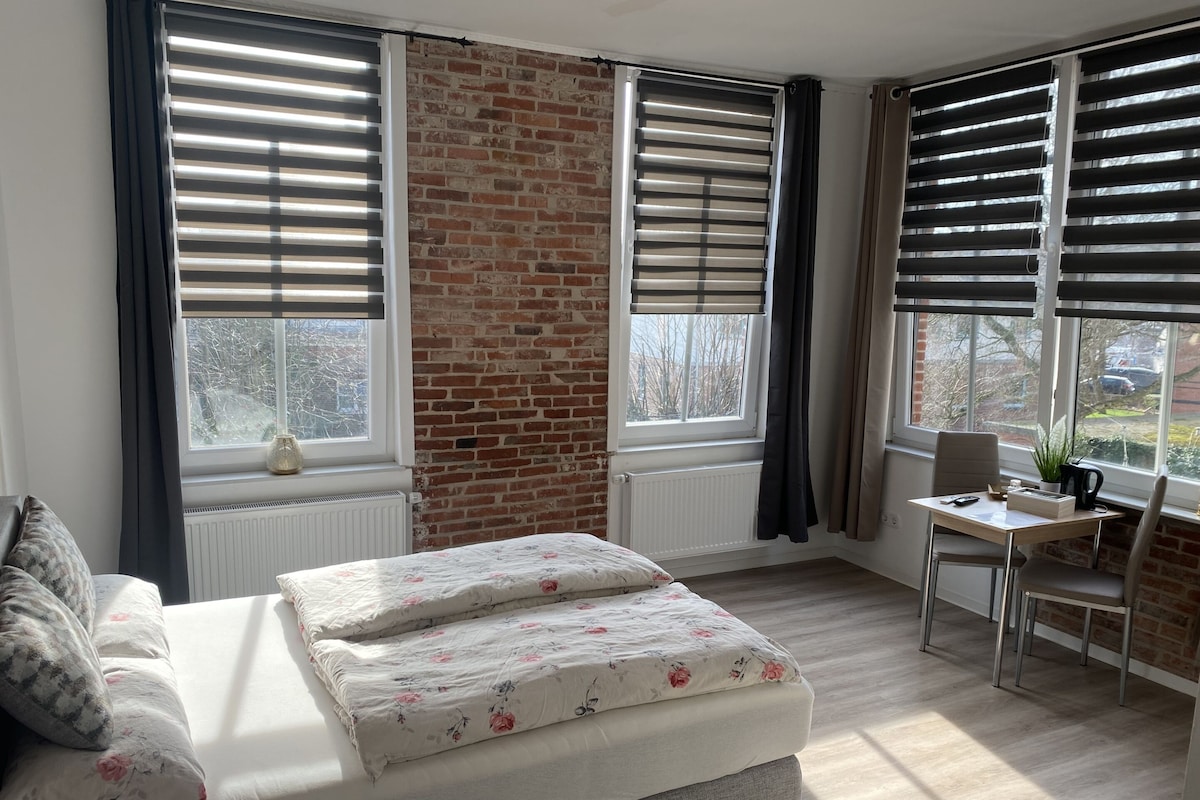 Quarto com cama, escrivaninha e vista para o exterior.