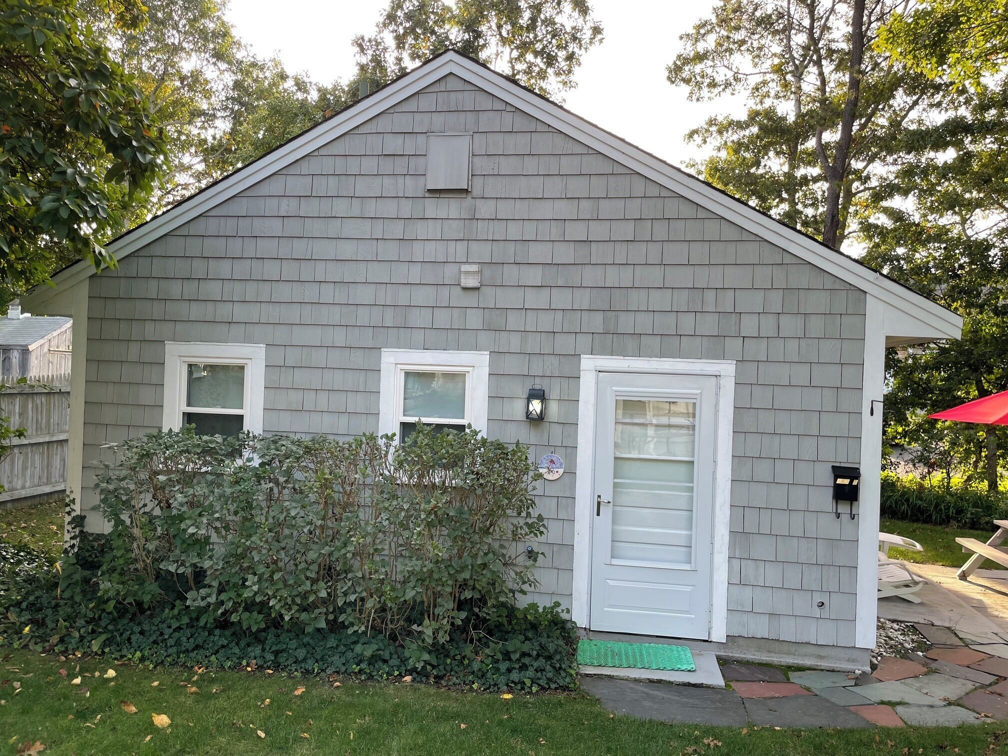 A small, single-story building with a gray shingled exterior, a white door, and a small window.