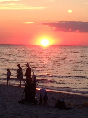 A sunset over the ocean with people on the beach.