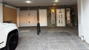 Ett garage med en vit SUV parkerad inuti, en stÀngd garagedörr och en stenmur med en dörr som Àr mÀrkt med nummer 50.