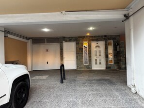 A garage with a white SUV parked inside, a closed garage door, and a stone wall with a door marked with the number 50. - 🏠 Zografou Urban Nest! (Zografou)