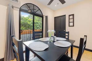 Uma sala de jantar com mesa, cadeiras, um vaso com flores e vista pela porta de vidro.