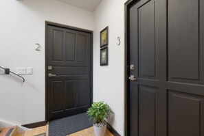 Um corredor com uma porta escura com o número 2, um vaso de planta e uma porta com o número 3.