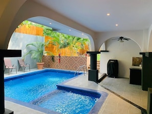 Une piscine avec vue sur la végétation tropicale, un ventilateur de plafond et un petit coin cuisine.