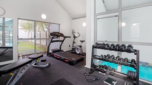 Un gimnasio con cintas de correr, elípticas y un estante con mancuernas.