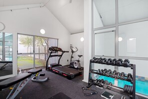 Un gimnasio con cintas de correr, elípticas y un estante con mancuernas.