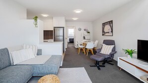 Una sala moderna con sofá, sillón y mueble para televisor. Cuenta con un comedor con mesa y sillas, además de una cocina con refrigerador.
