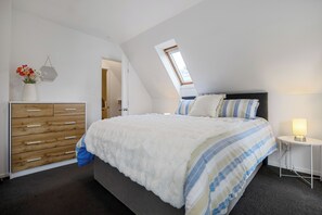 Ein Schlafzimmer mit Bett, Schminktisch, Nachttisch und Dachfenster.