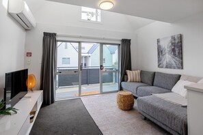 Ein modernes Wohnzimmer mit grauem Sofa, einem Flachbildfernseher, einem gewebten Ottomanen und einem Bild an der Wand.