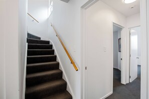 A staircase with carpeted steps and a wooden handrail, leading to a white door. - Urban Oasis - Christchurch Holiday Home (Christchurch)
