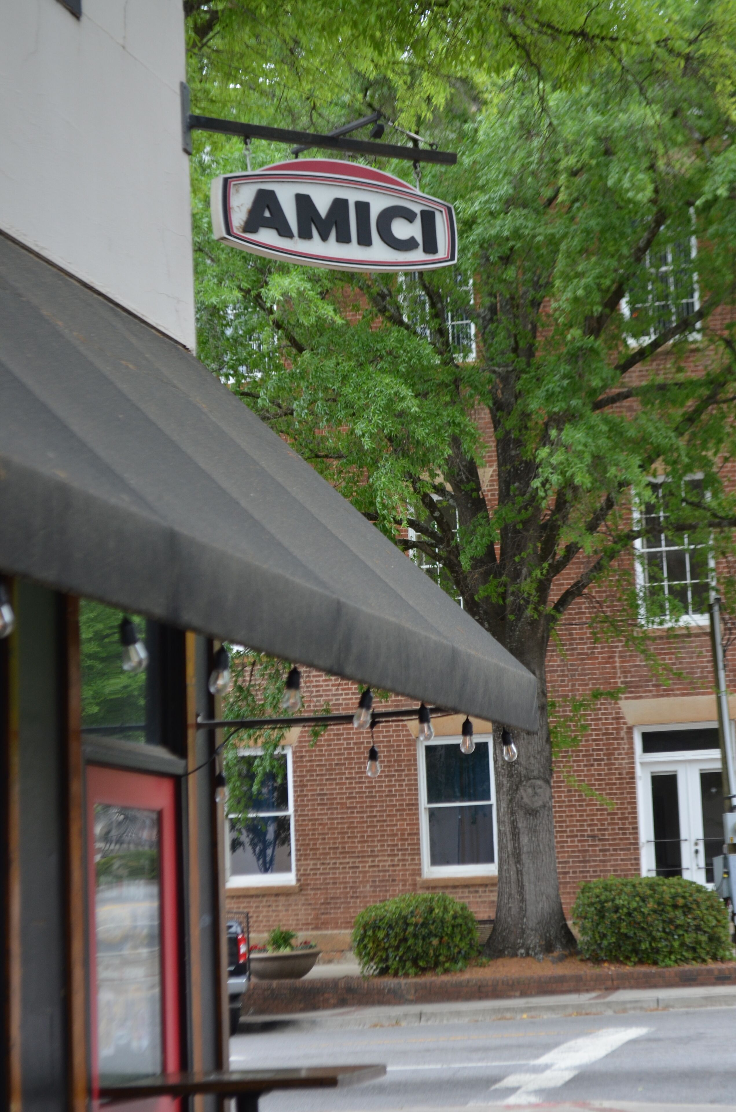Une devanture de magasin avec une enseigne portant l’inscription « AMICI » et un arbre devant un bâtiment en briques.