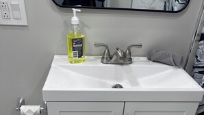 Un bagno con un lavandino bianco, uno specchio, una bottiglia di sapone per le mani e un asciugamano.